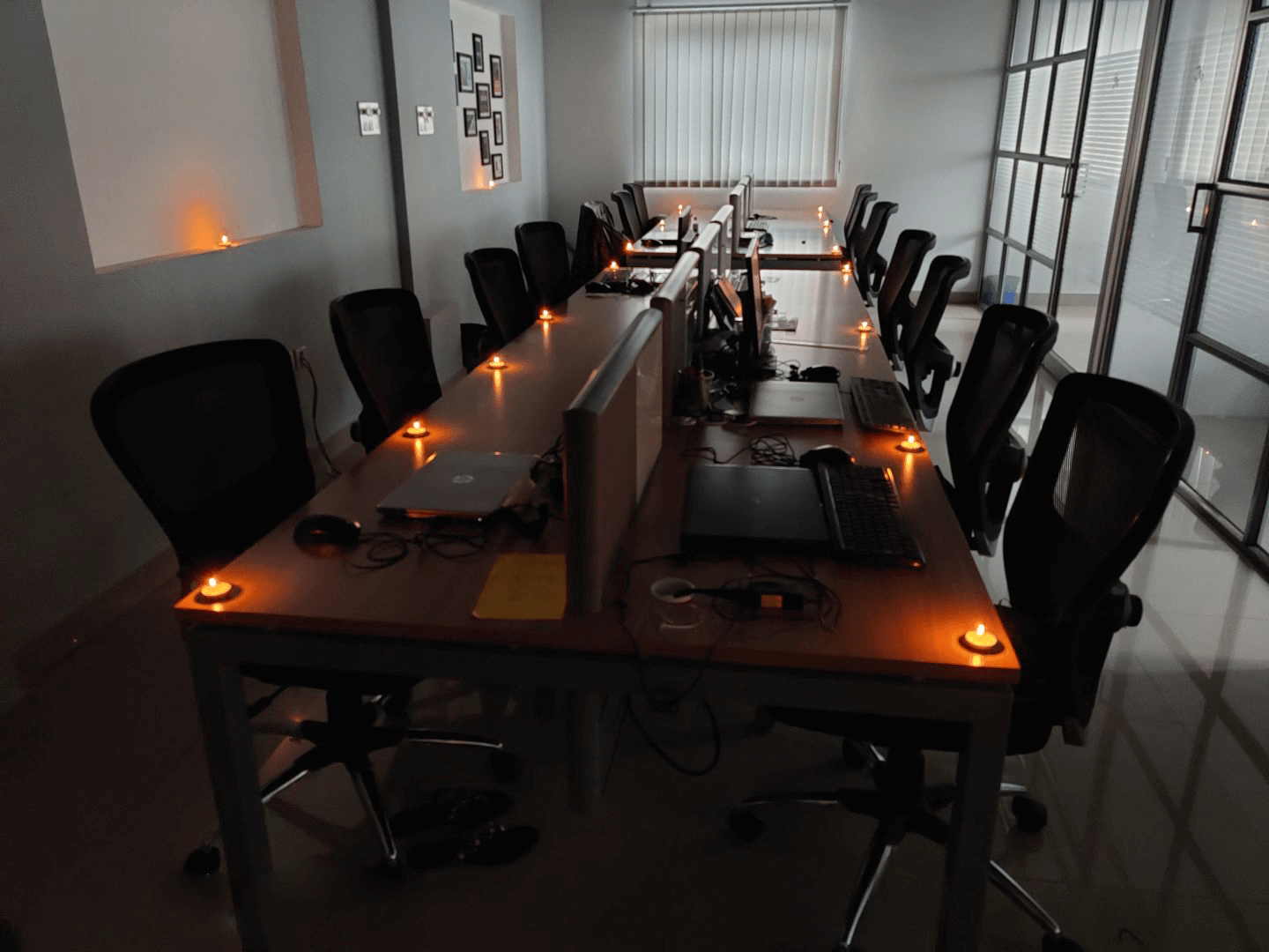 A modern office workspace with long desks, computers, and chairs, lit by small candle lights.